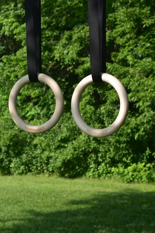 Calisthentials wooden gymnastics rings hanging from black straps outdoors in front of green trees